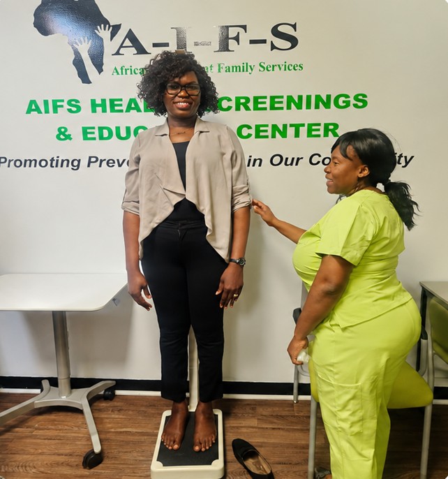 An AIFS health worker measuring a smiling client’s height in front of the Health Screenings and Education Center sign