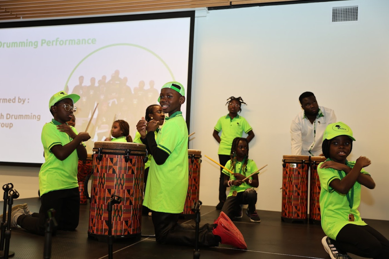 Youth drummers in AIFS caps and shirts performing on djembe drums on stage